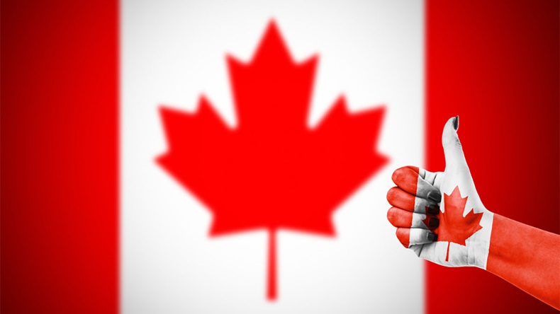 Hand, painted with the flag of Canada, giving thumbs up sign with flag of Canada in background