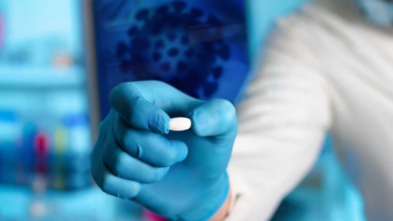 Oral tablet being held up by person in blue medical gloves and lab coat