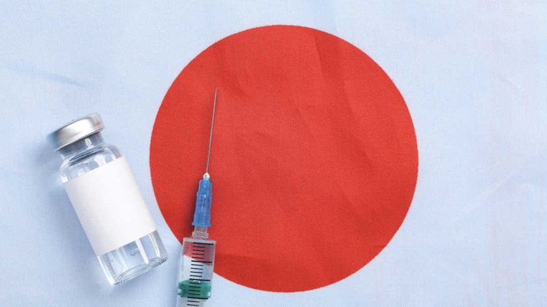 Vial and syringe laid out on top of a Japanese flag