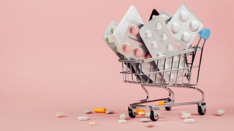 Miniature shopping cart of pill packets on pink background