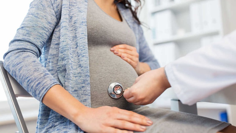 Closeup of doctor applying stethoscope to pregnant woman's belly