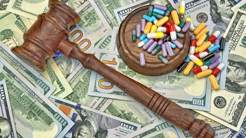 A gavel and hammer on top of US bank notes. Gavel is covered in a range of pill capsules.