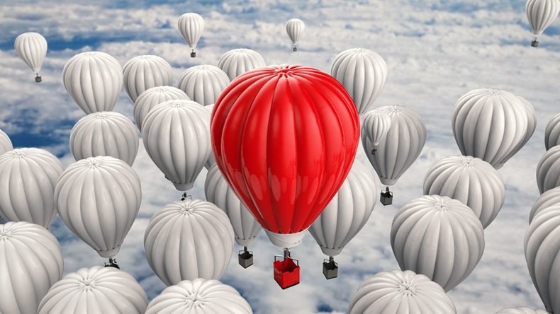 A red hot air balloon standing out in a sea of white hot air balloons