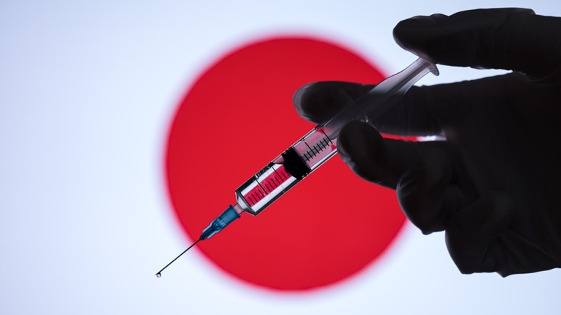 Gloved hand holding injectable syringe in front of Japanese flag