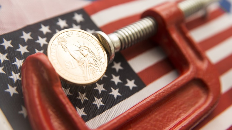 Dollar coin squeezed in G-clamp on top of USA flag