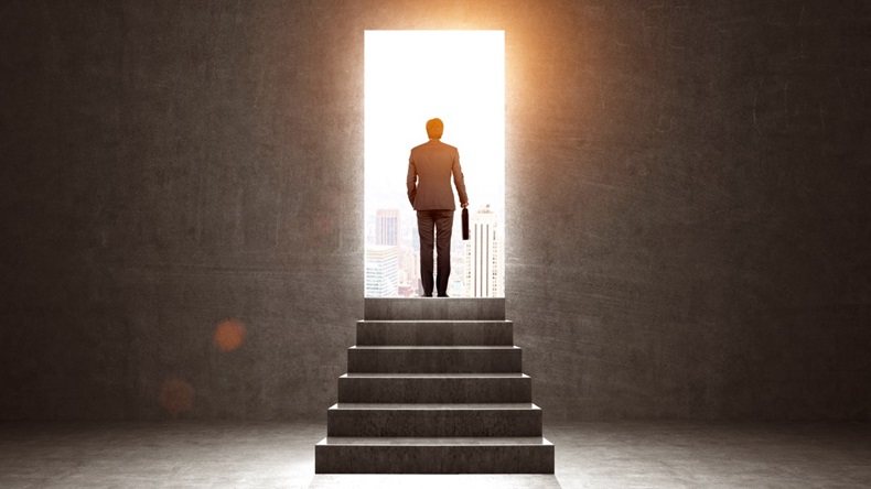 Rear view of businessman in suit standing at the top of steps in front of a lit doorway; fresh start concept