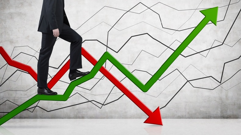 Businessman walking up ascending green graph while descending green graph hovers in background