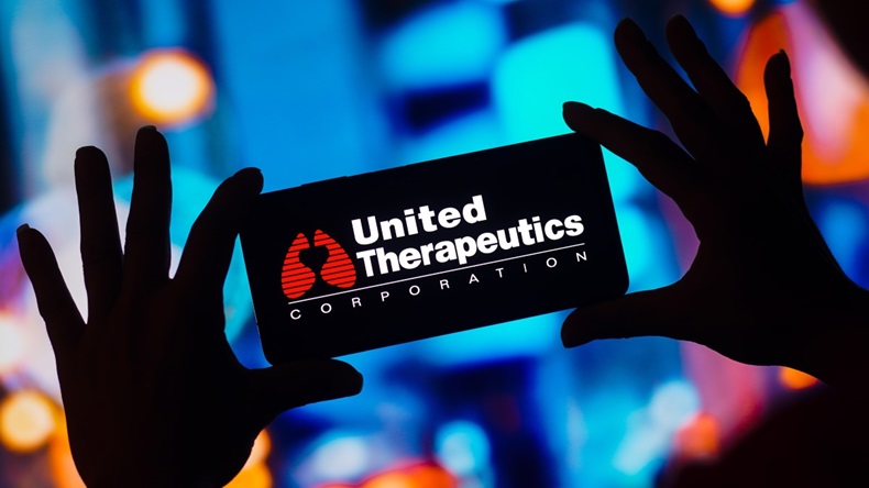 Logo of United Therapeutics on smartphone, held by hands in silhouette